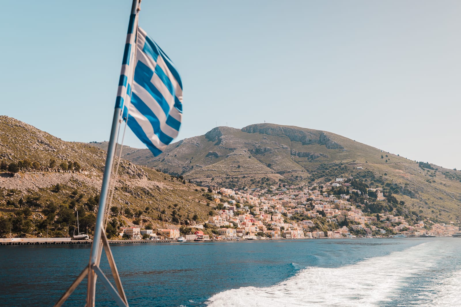 greece flag and colourful buildings on a hillside next to the sea - Symi Island, greece
