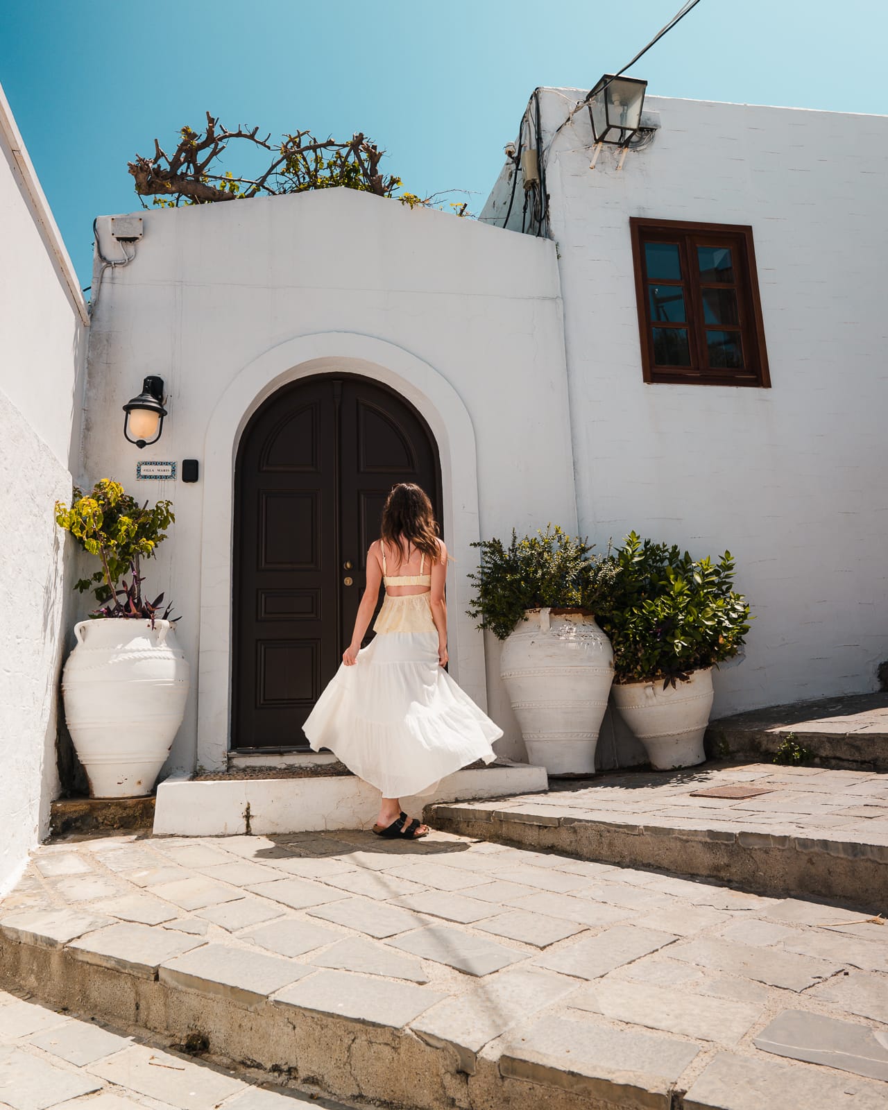woman standing infront of white building and brown doorway in lindos, greece