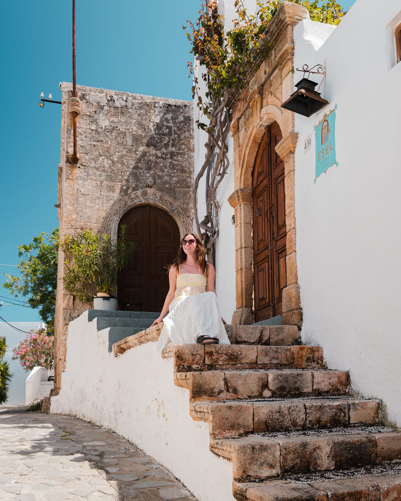 woman sitting on stone steps infront of door in lindos, greece