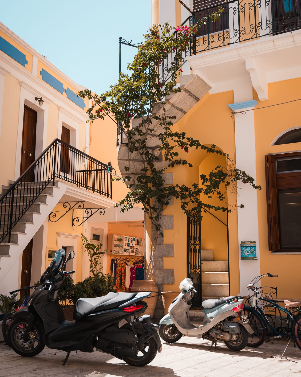 yellow building with spiral staircase with green ivy plants and motorbike at symi island, greece
