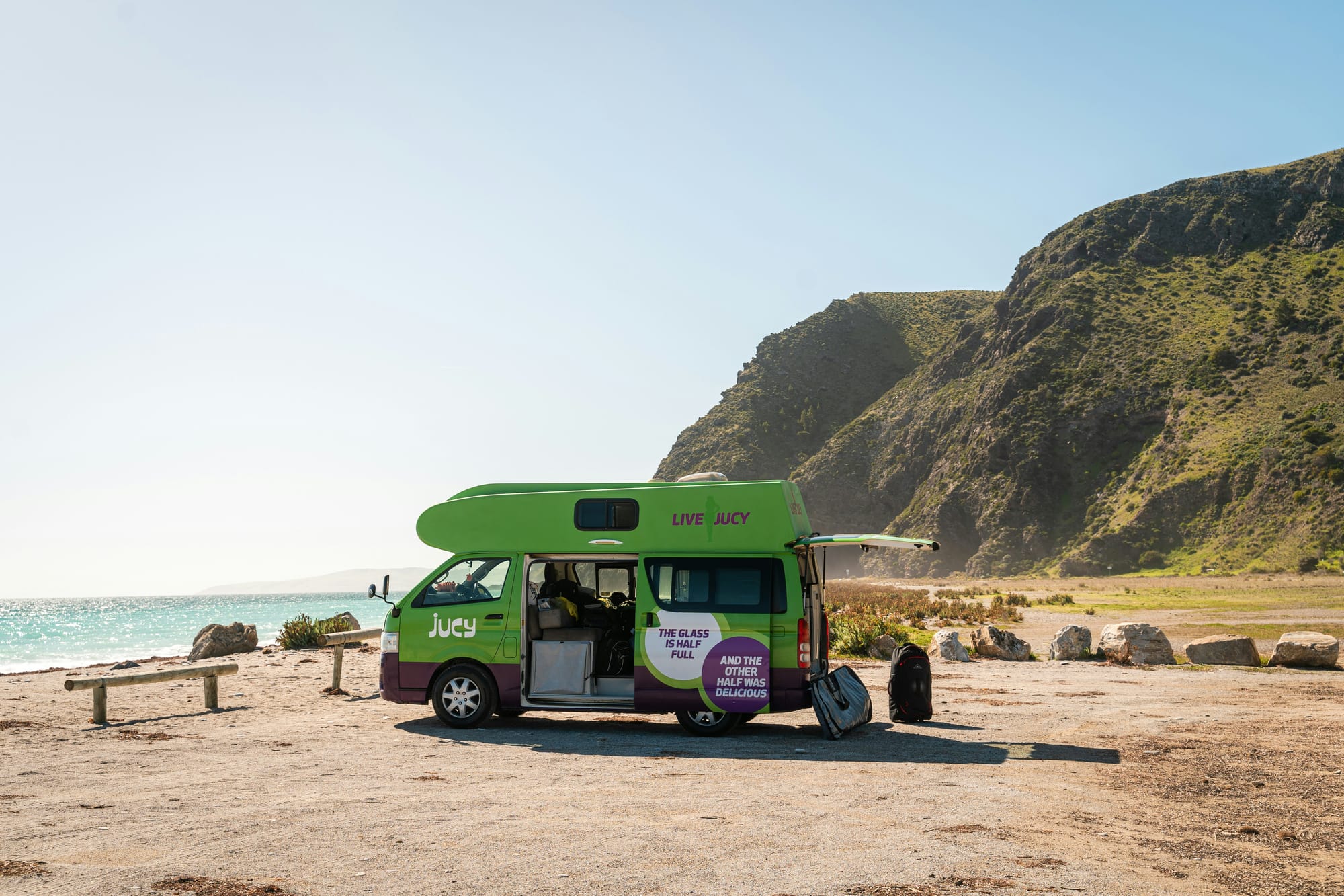 jucy campervan parked next to beach with mountains behind, in new zealand
