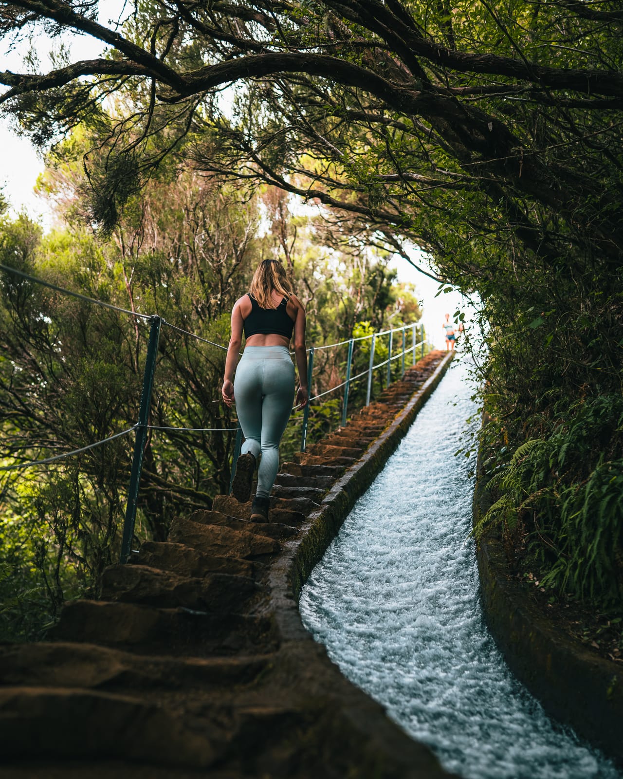 woman waling up steps next to a levada on the 25 Fontes hike in madeira