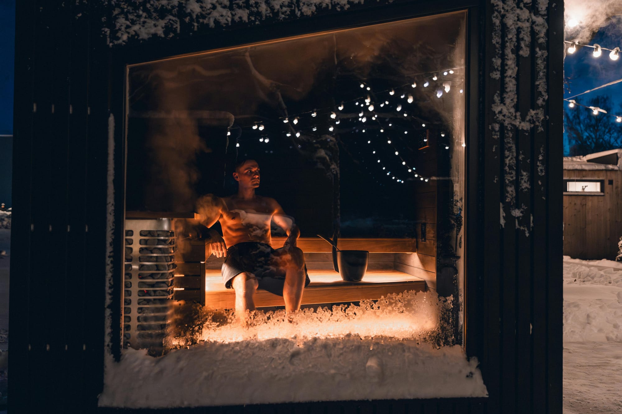 man sitting in a sauna in winter, with snow and ice on the outside
