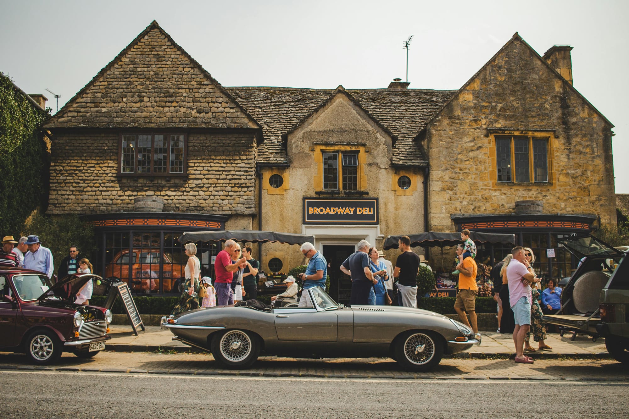 cars and people standing outside of Broadway Deli in the Cotswolds