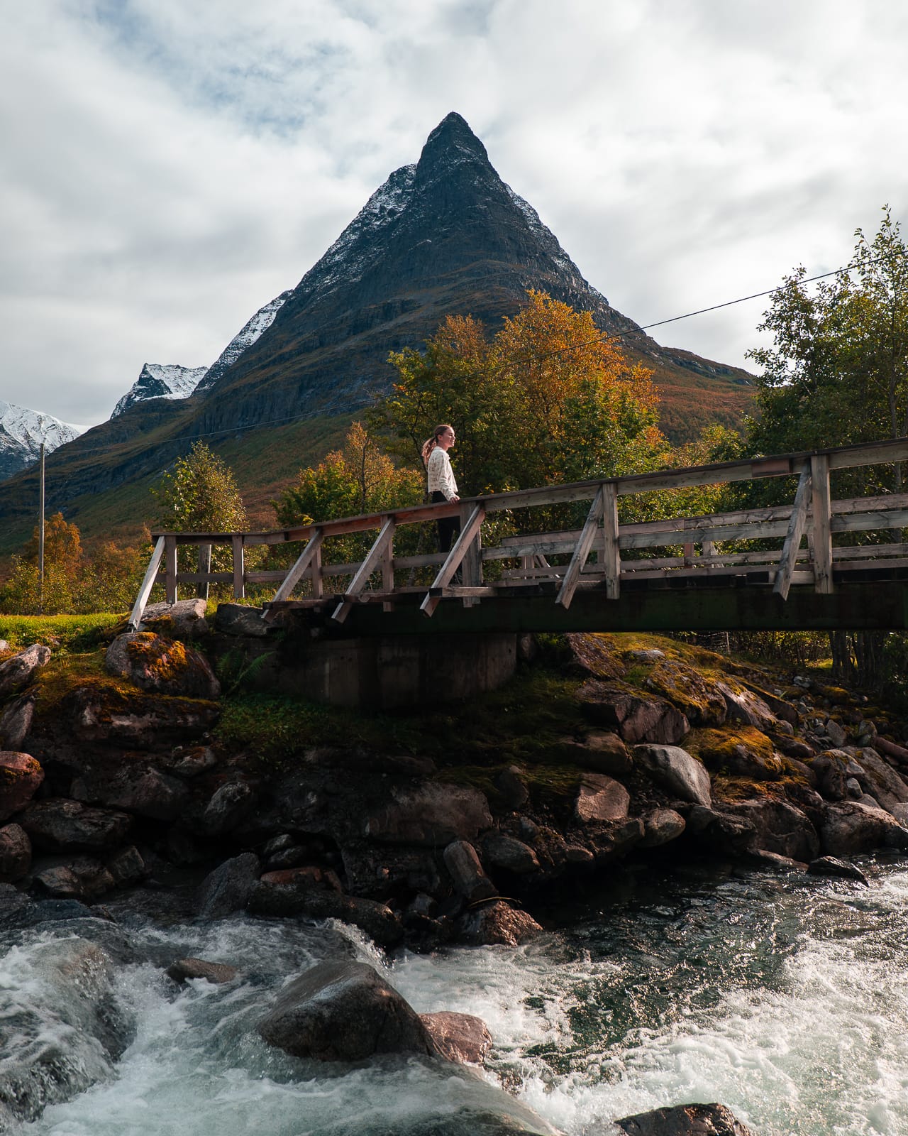 woman standing on bridge over river with mountain in background in Innerdalen Valley