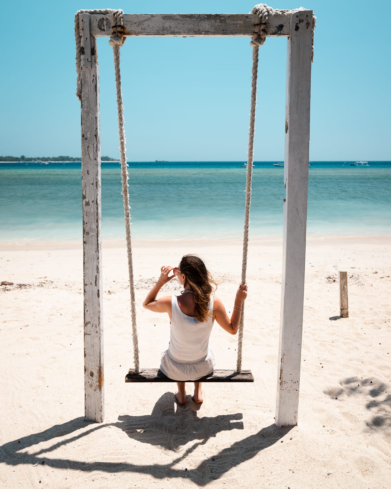woman sitting on swing at beach with white sand and turqoise water on Gili Air