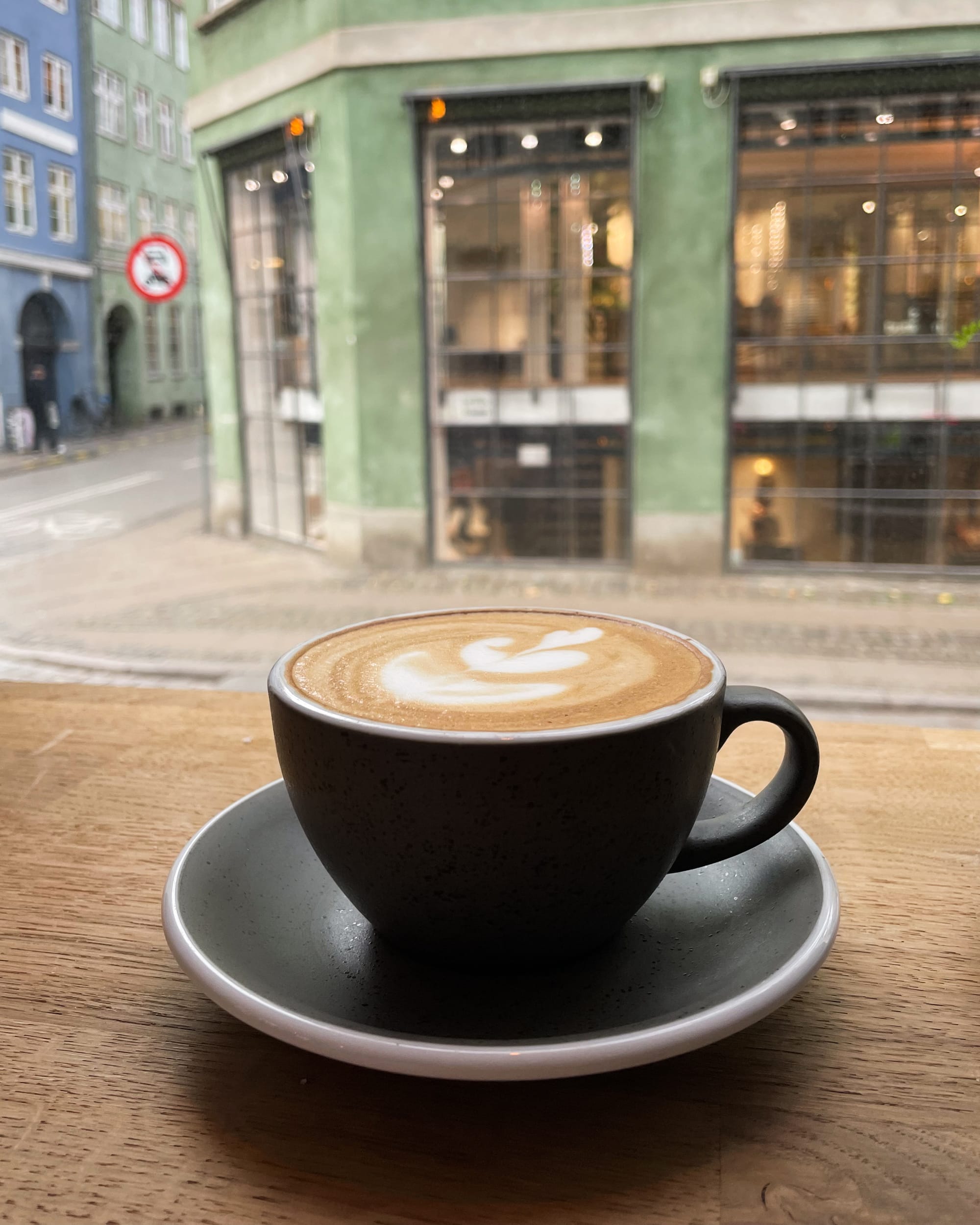 black mug of coffee infront of a window at a cafe in copenhagen