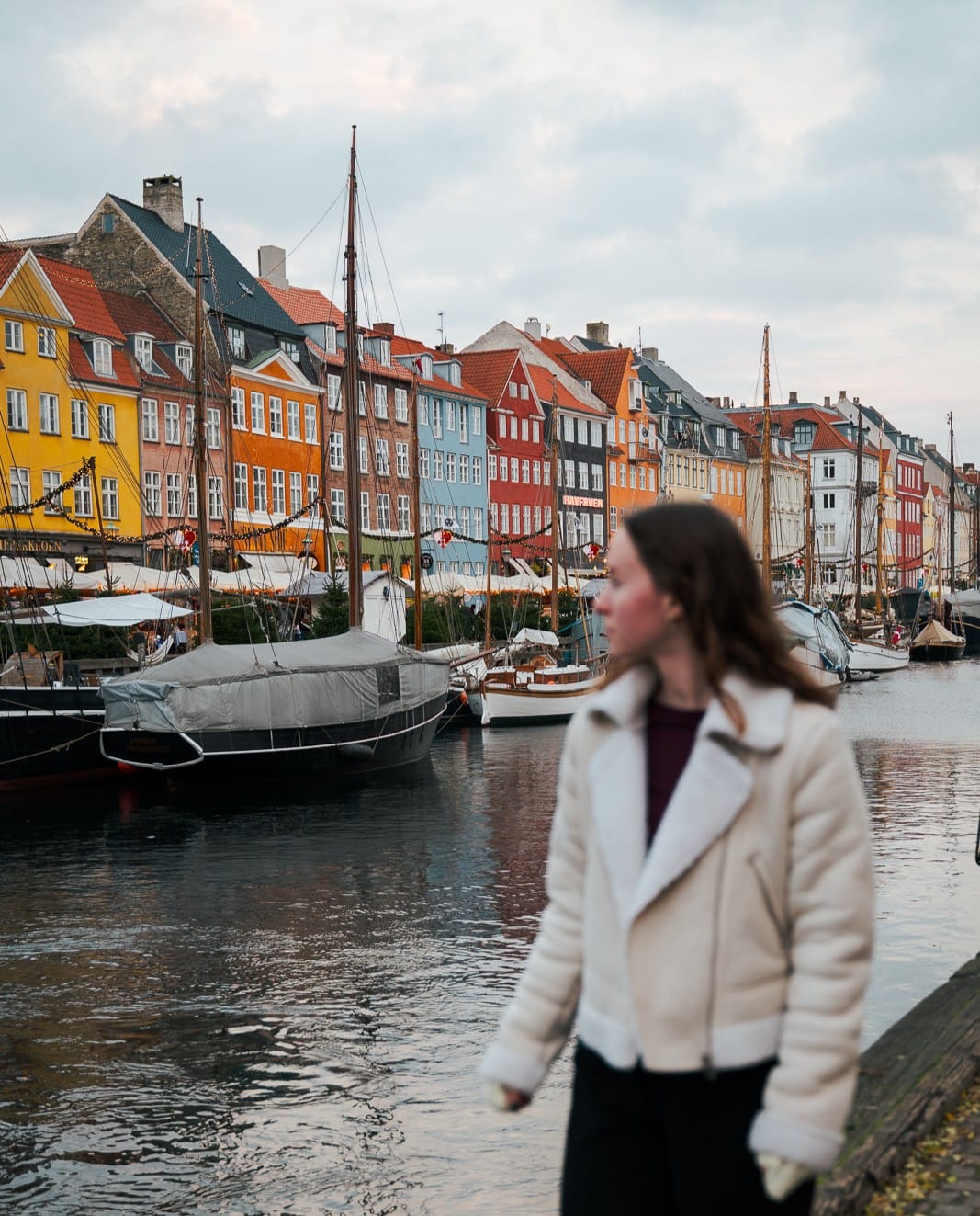 woman standing next to canal and colourful houses in Nyhavn, Copenhagen