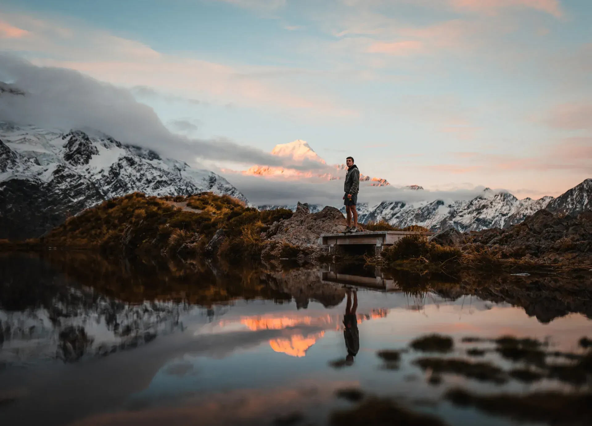 Reflection of a hiker and Mt Cook in Sealy Tarns at sunset in New Zealand
