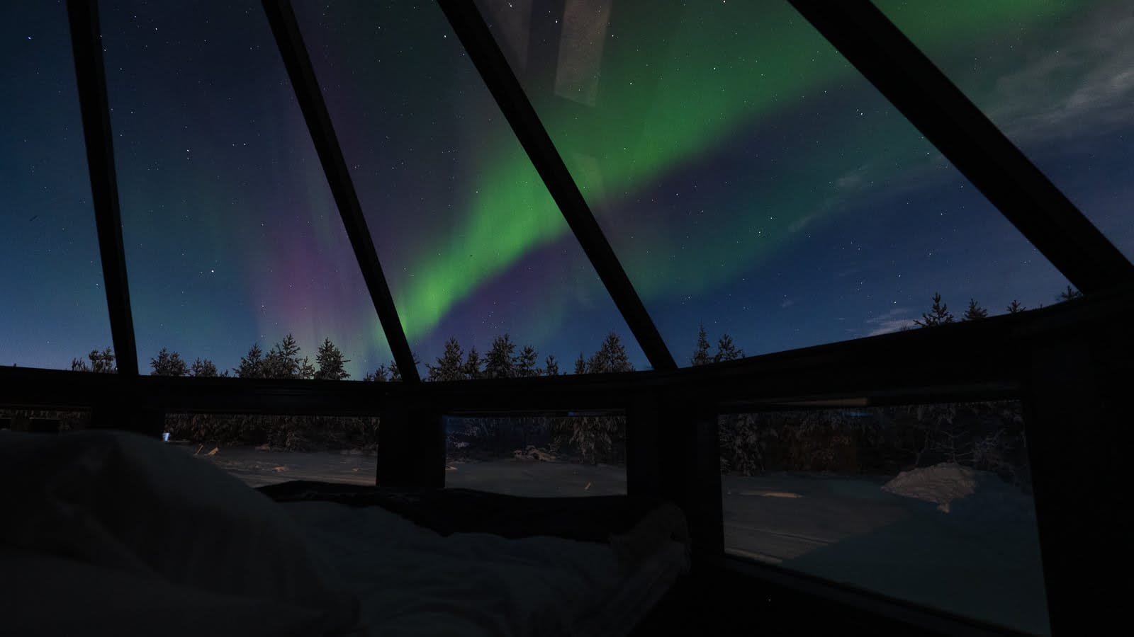 Aurora northern lights view from bed through a glass cabin at Northern Lights Village, Lapland